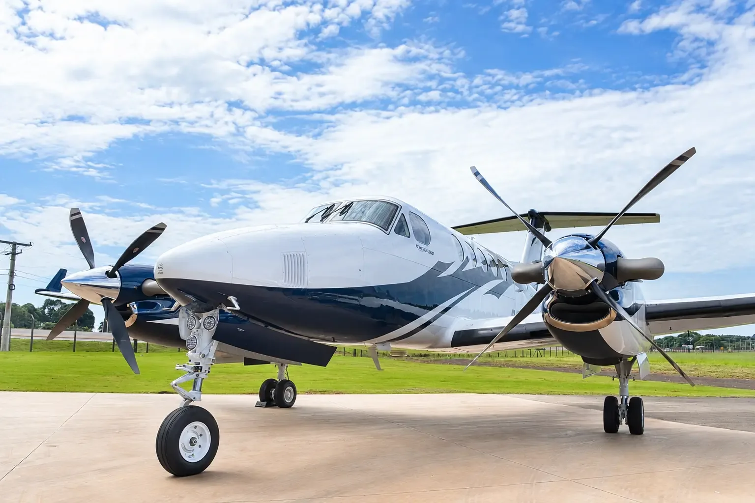 A front view of a white and blue twin-turboprop aircraft with its propellers visible, parked on a tarmac.