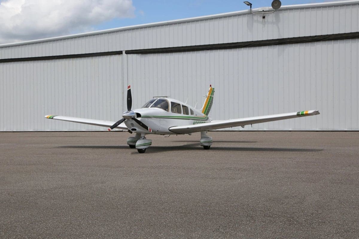 Side front view of a white and green Piper Dakota aircraft on the tarmac.