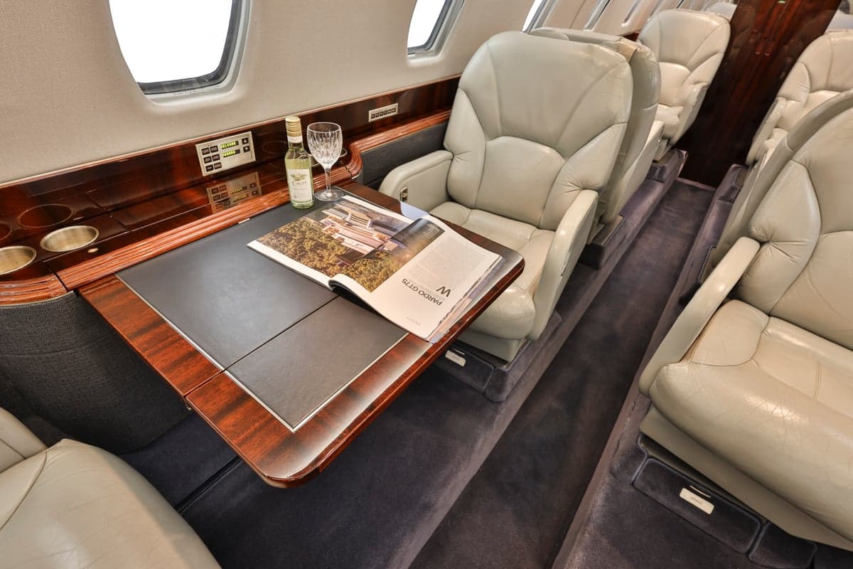A close-up of the table inside a Citation CJ3 aircraft, showing a magazine, wine bottle, and leather seats.