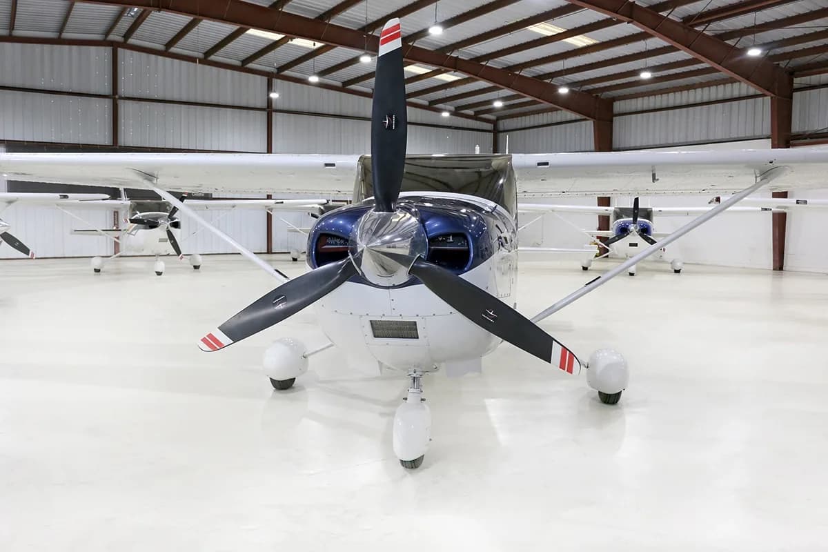 A white and blue Cessna Skylane N890MB is parked in a hangar, viewed from the front.