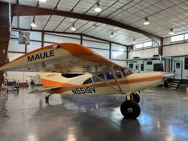 A Maule aircraft with registration N5519V, painted white and orange, parked inside a hangar.