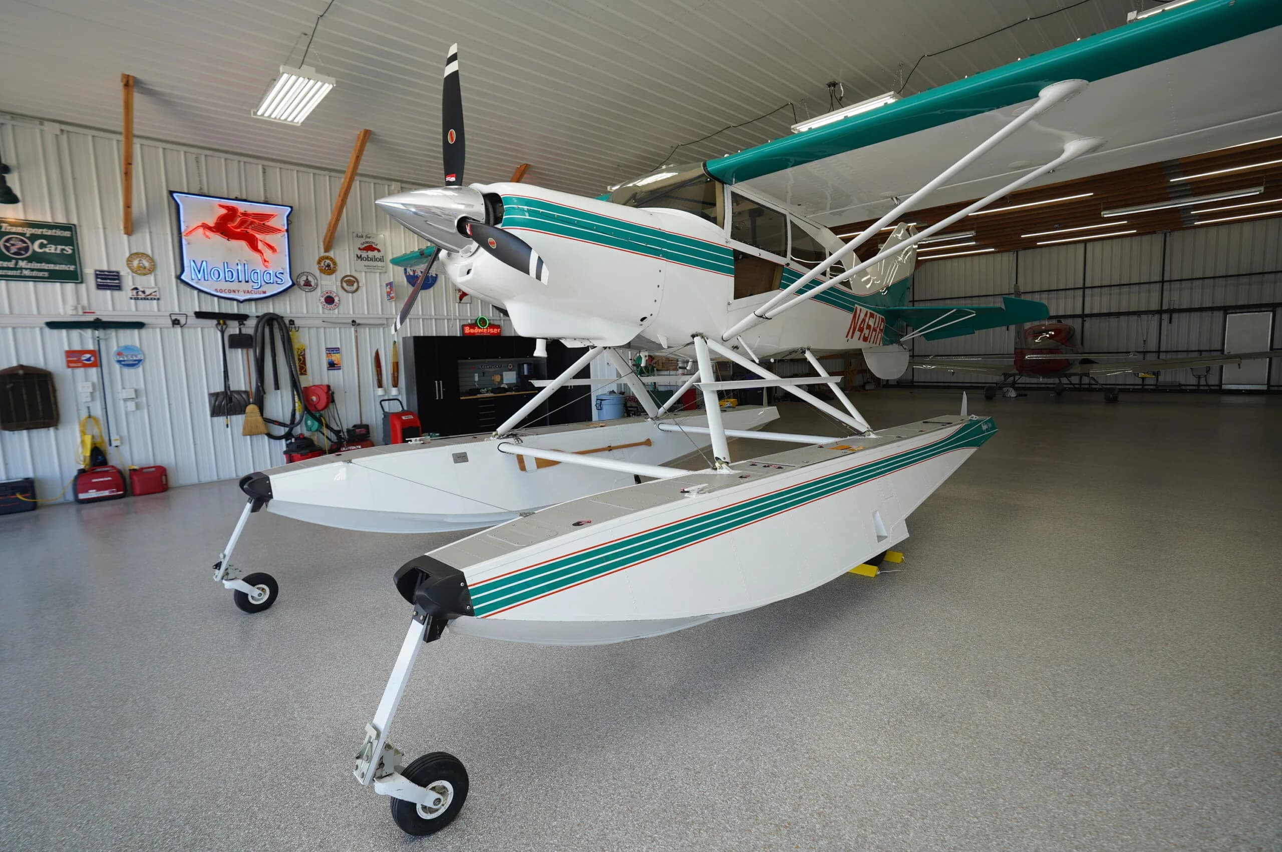 Front-left view of a white and teal floatplane with wheels, parked in a hangar.