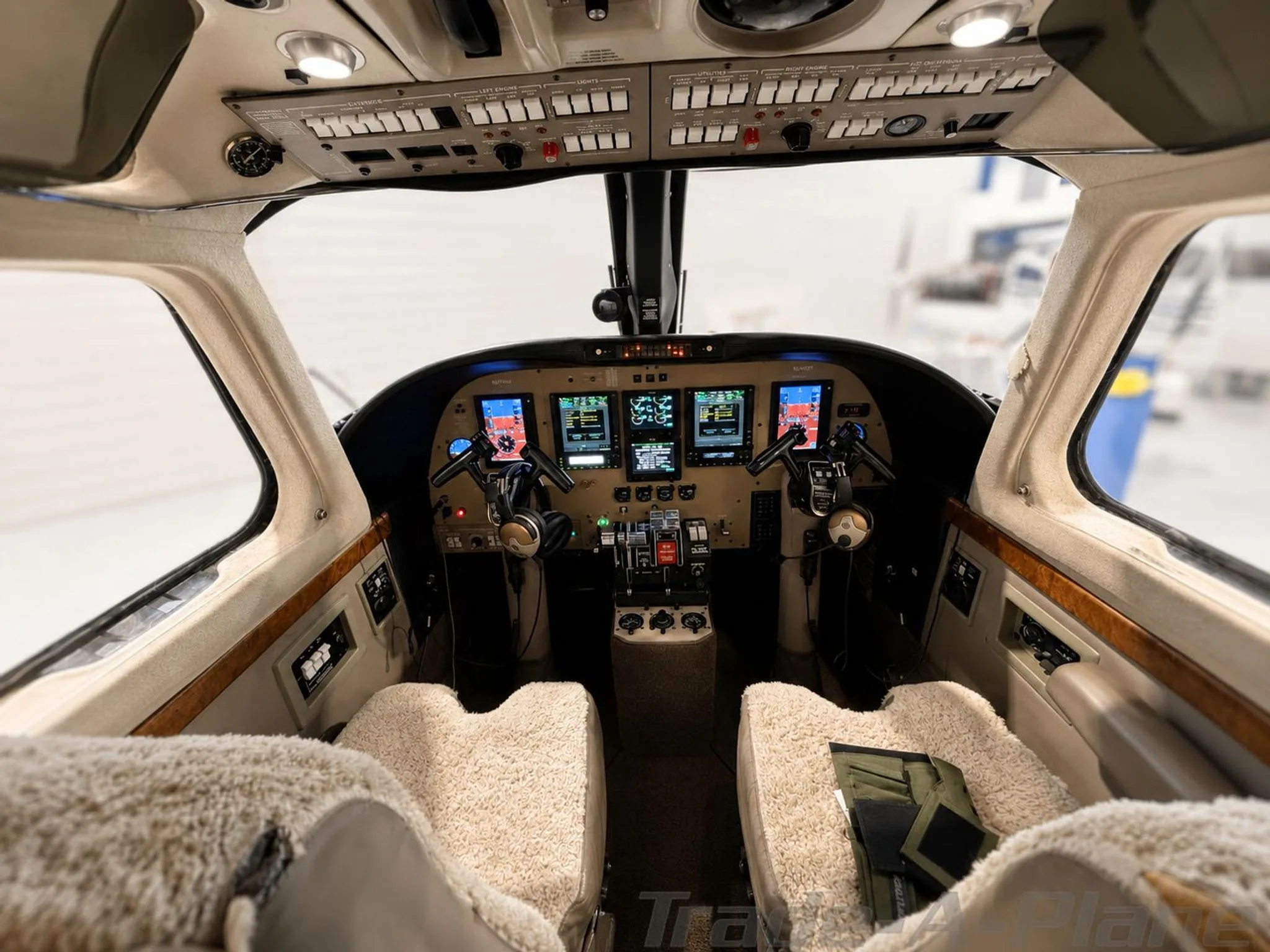 The cockpit of a twin-engine turboprop aircraft with modern glass displays and sheepskin seat covers.