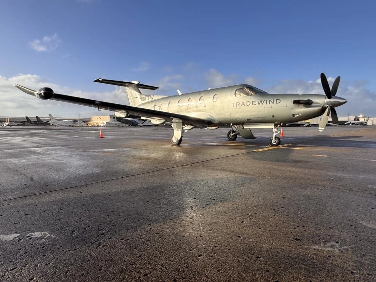 A Tradewind PC-12 aircraft, registration N881TW, parked on the tarmac with a blue sky background.