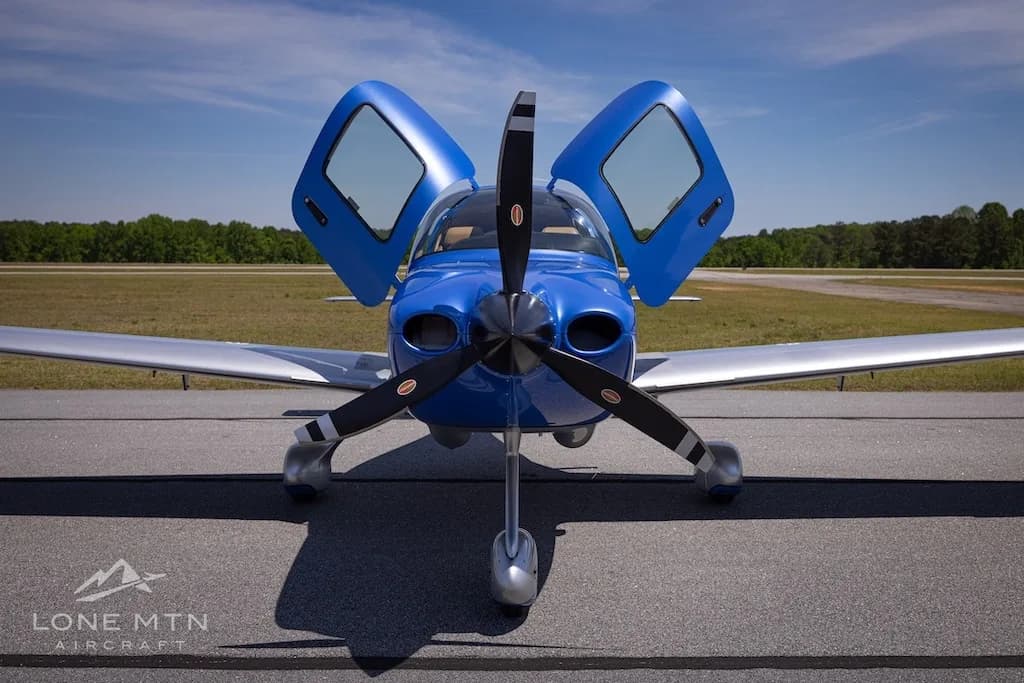 A head-on view of the blue and silver Cirrus SR20 aircraft (N251SR) with its doors open, parked on an airfield.