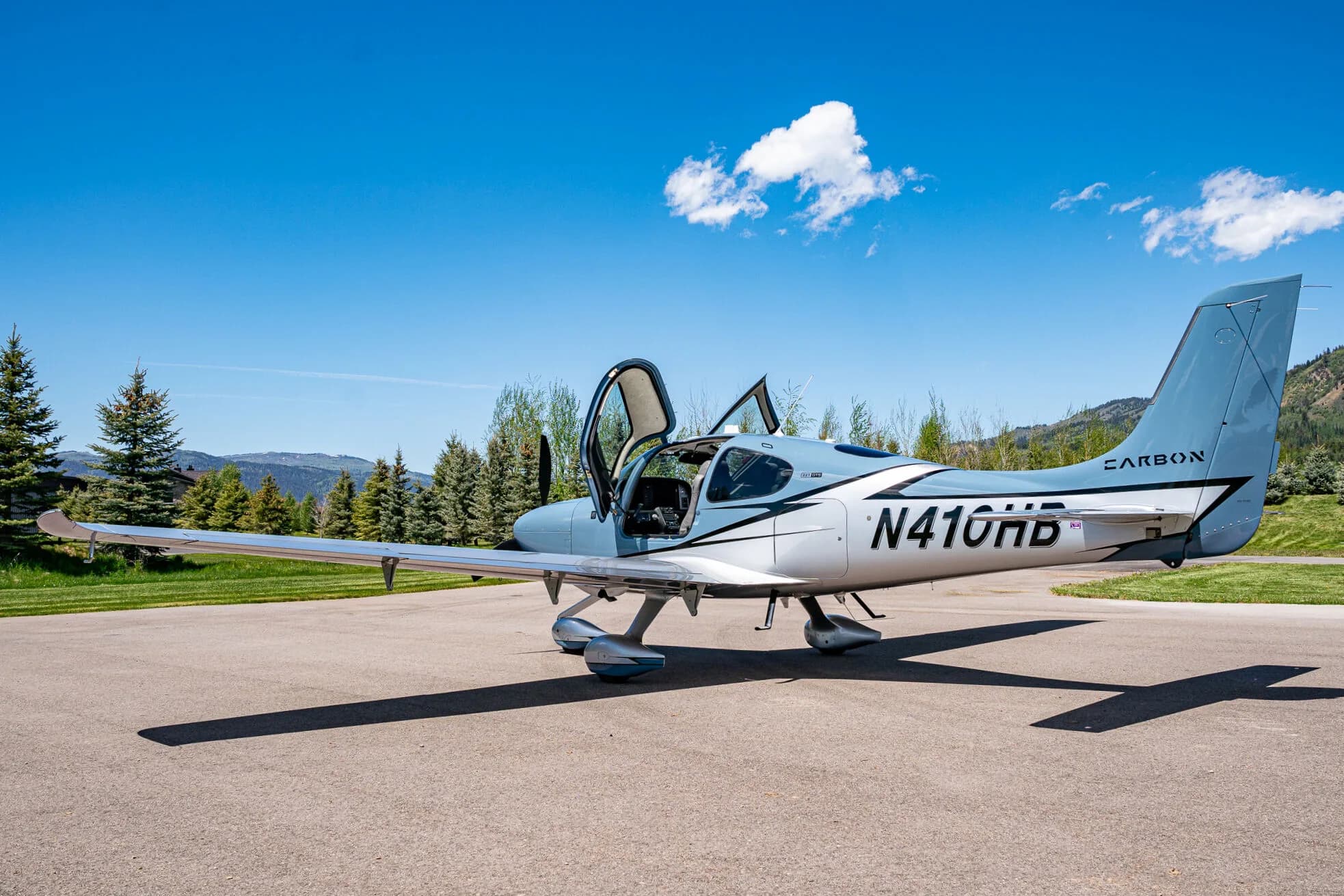 A light blue and silver Cirrus SR22T aircraft (N410HB) with its doors open, parked on an airfield.