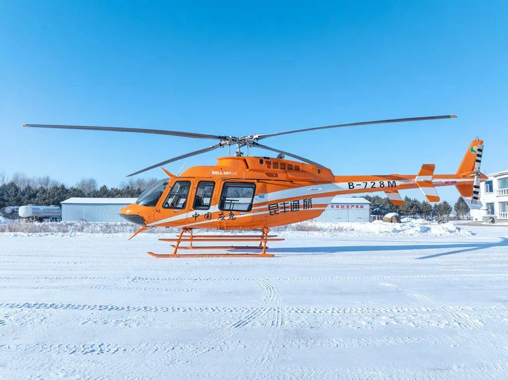 A side view of an orange and white Bell 407 helicopter with registration B-728M parked on a snow-covered field.