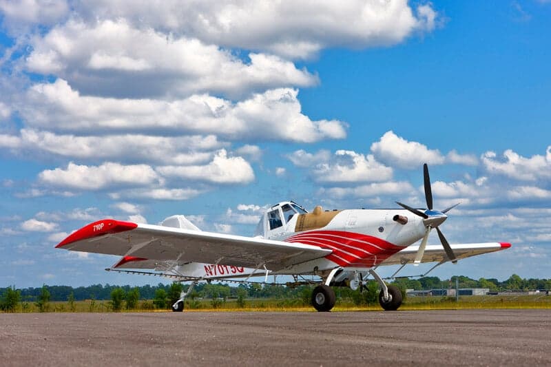 A white and red agricultural aircraft, N7015Q, is parked on an airfield under a bright blue sky with white clouds.