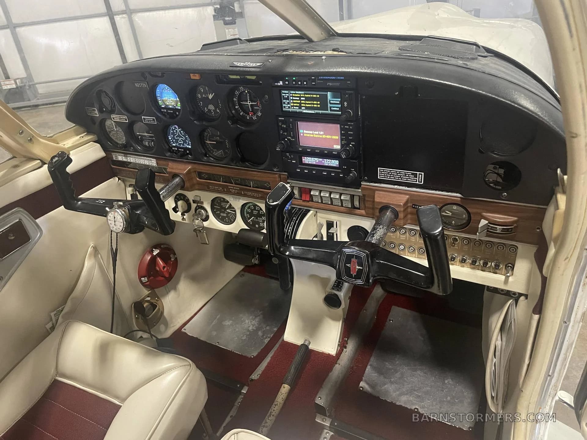 The cockpit of a single-engine aircraft, showing the instrument panel with avionics, yokes, and red and white interior.