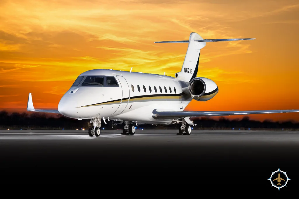 A white and gold business jet (N62AE) on a tarmac at sunset.