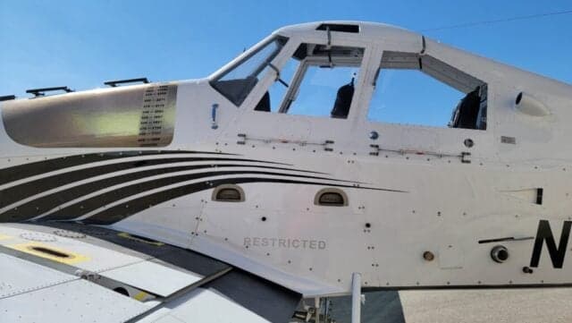 Close-up side view of a white agricultural aircraft's cockpit and fuselage with black stripe livery.
