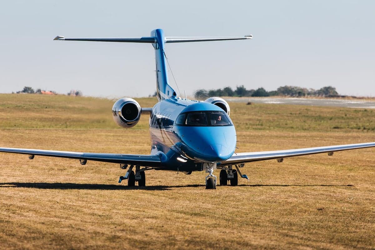 A blue Pilatus PC-24 taxiing on a grassy field.