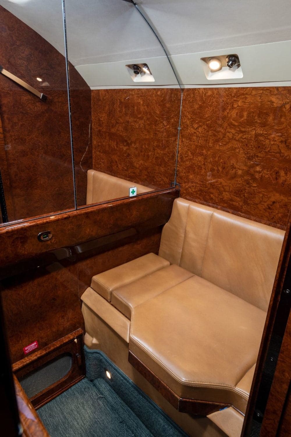 A tan leather bench seat with wood paneling and a mirror in an aircraft cabin.