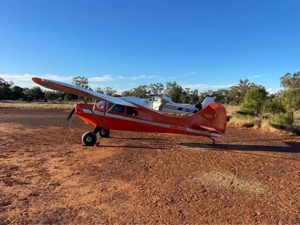 An orange and white high-wing aircraft with tail number 24-8804 parked on a red dirt field under a clear blue sky.