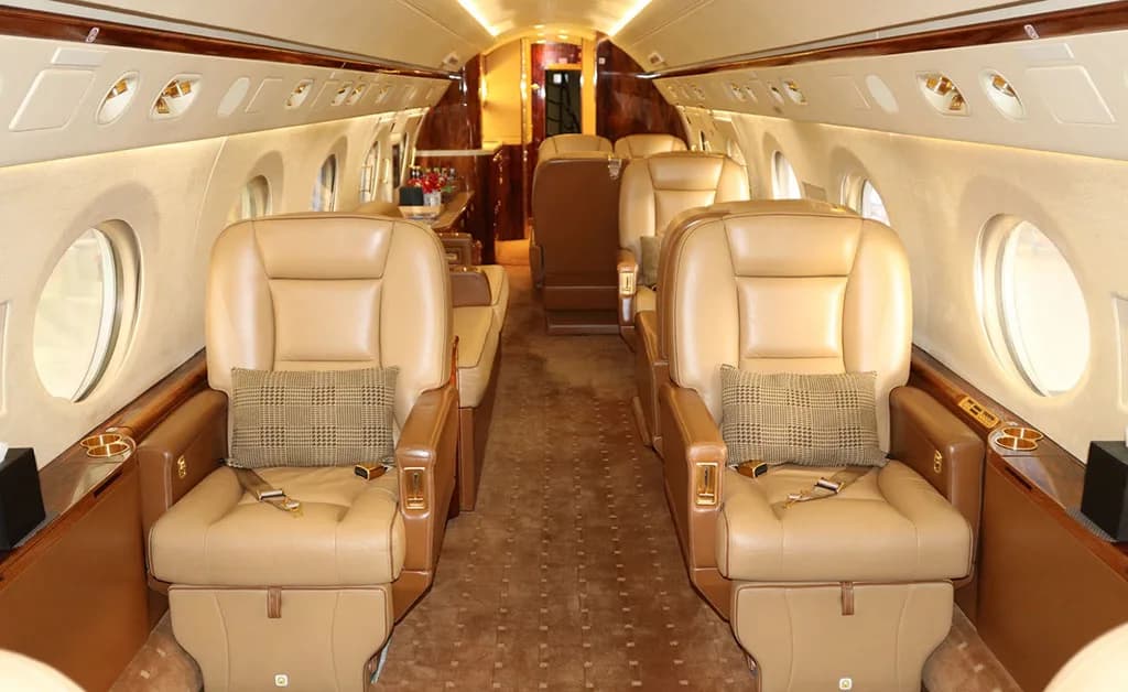 The luxurious interior cabin of a private jet, featuring tan leather seats and wood accents.