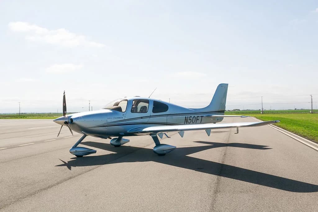 A side view of the light blue Cirrus SR22 aircraft with its doors closed, parked on an airfield.