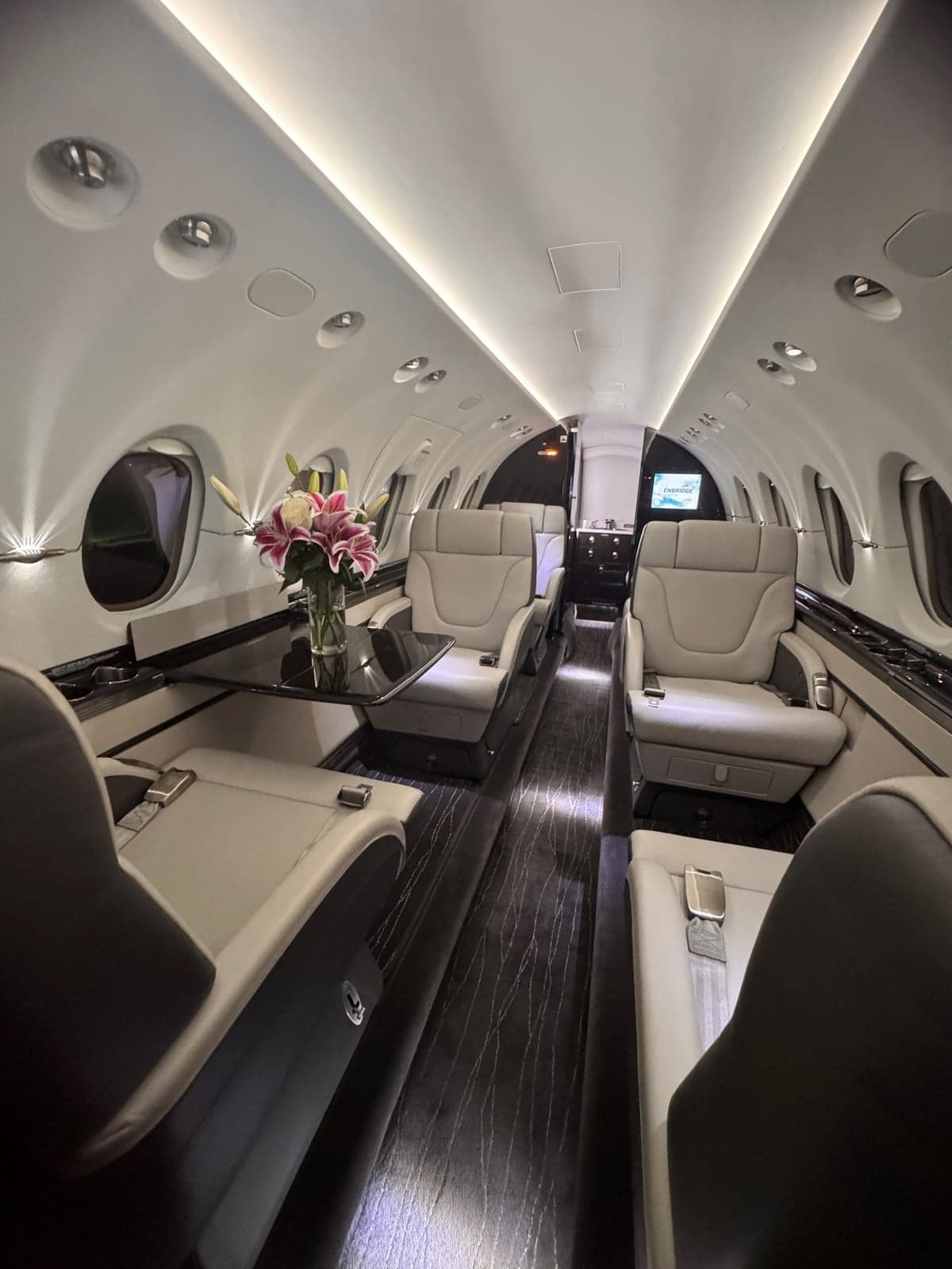 View of the aircraft's interior cabin with light-colored seats and a table with flowers.