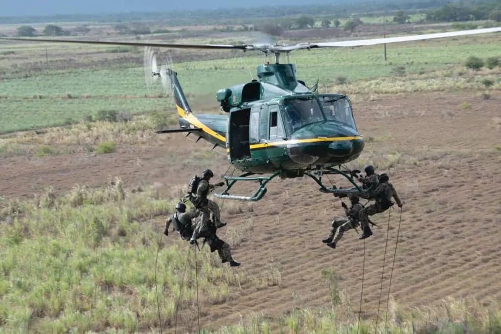 Bell UH-1 Iroquois helicopter with people rappelling from it over a field.