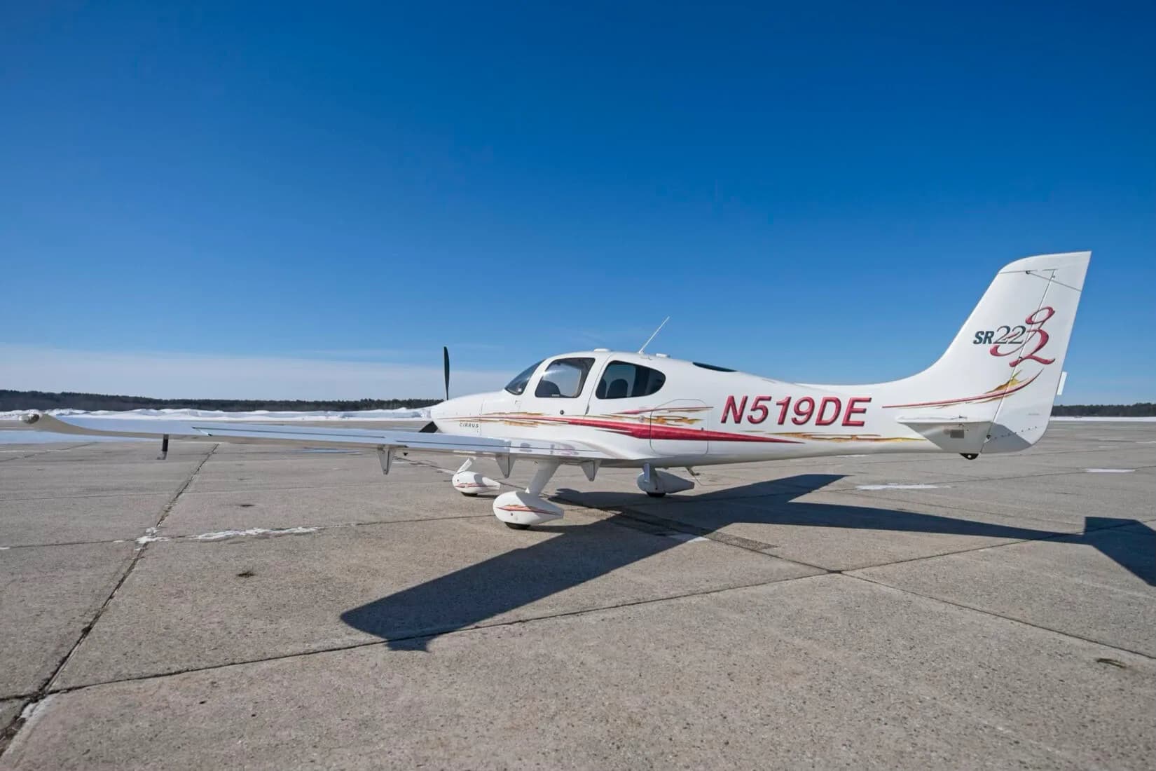 A white Cirrus SR22 aircraft with red and gold decals, registration N519DE, parked on a tarmac under a clear blue sky.