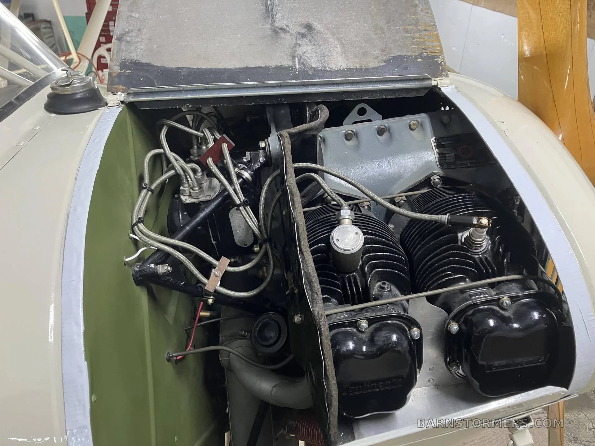 An overhead view of the exposed engine compartment of a light aircraft, showing the cylinders and various hoses.