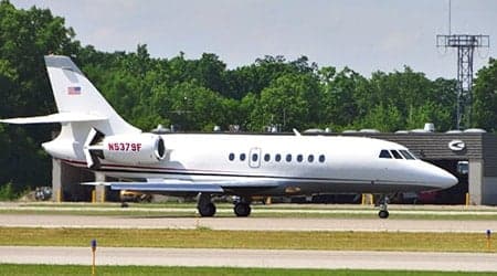 A white Dassault Falcon 900EX private jet (N5379F) with red and blue stripes, taxiing on an airport tarmac.