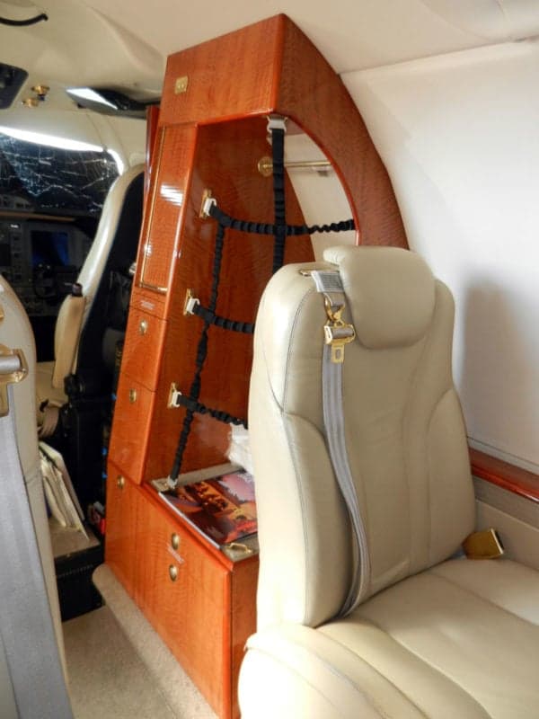 Interior view of a jet with a tan leather seat and wooden storage cabinet.