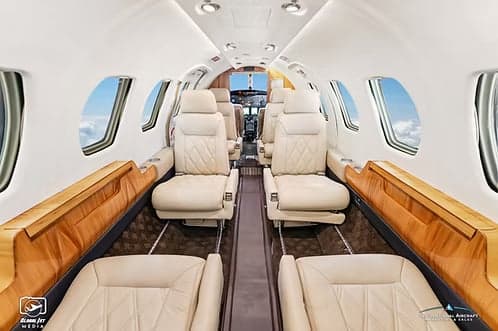 The spacious cabin interior of a business jet features light-colored leather seats and wooden side panels.