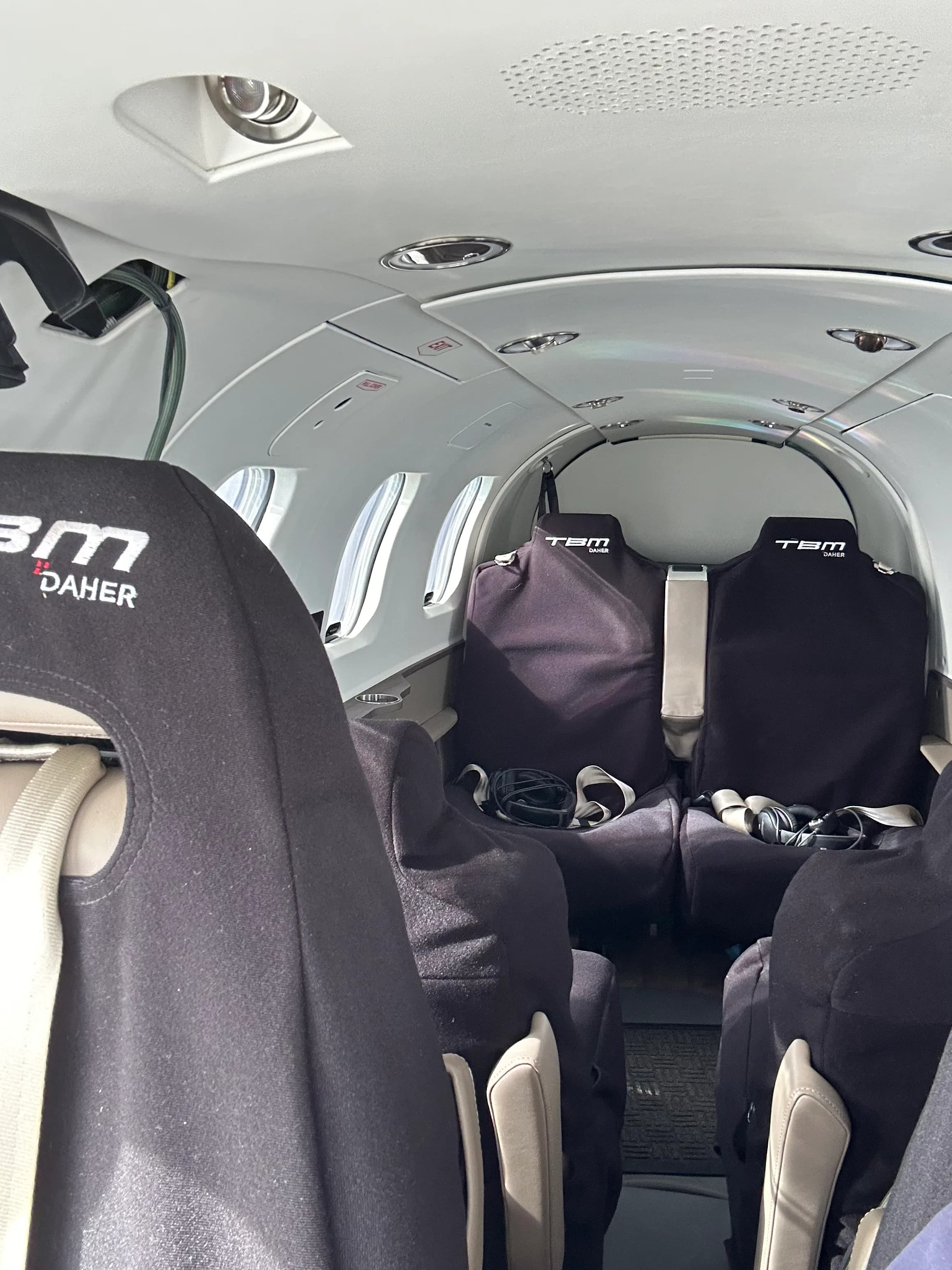 The interior cabin of a TBM aircraft, showing black seat covers with 'TBM DAHER' logos.