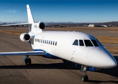 A white and blue Dassault Falcon 900EX, registration C-GEOS, parked on the tarmac.