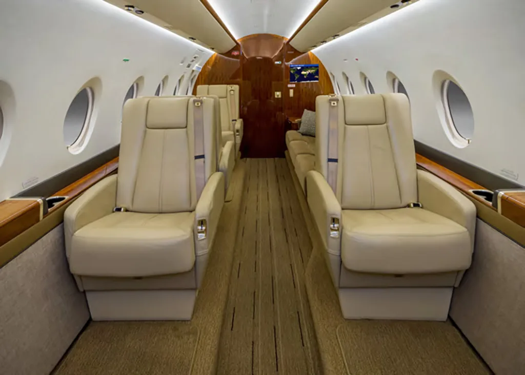 The aircraft's interior cabin features rows of beige leather seats and a wooden floor aisle.
