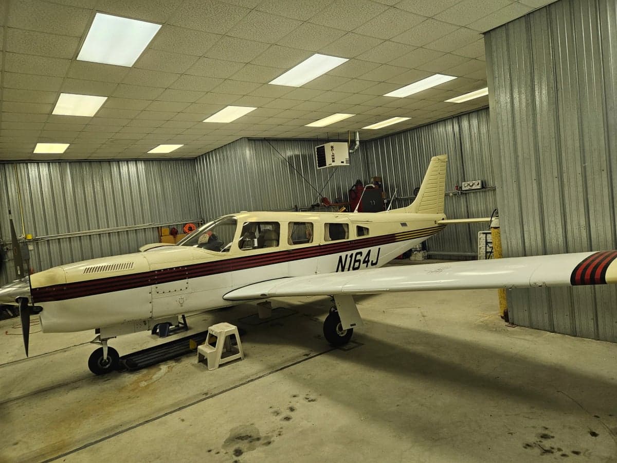 N164J, a light tan and white aircraft with red stripes, parked in a hangar.
