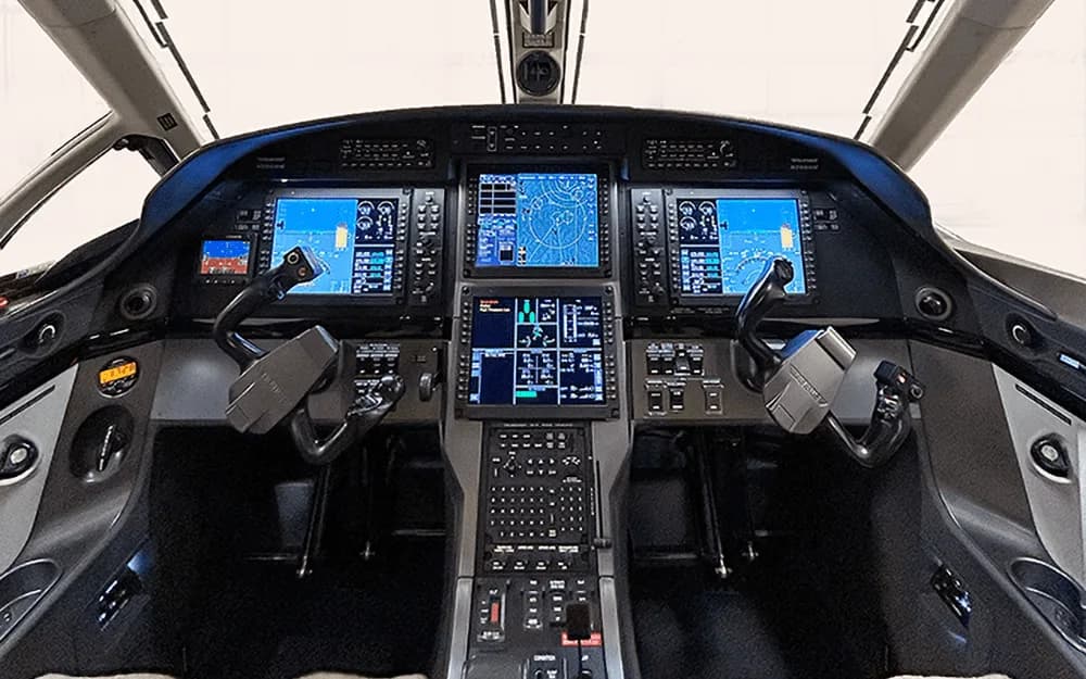 The modern glass cockpit of a Pilatus PC-12 NG, featuring multiple large display screens and control yokes.