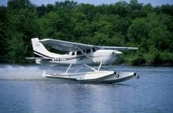 A white and black Cessna 206 on floats speeds across the water.
