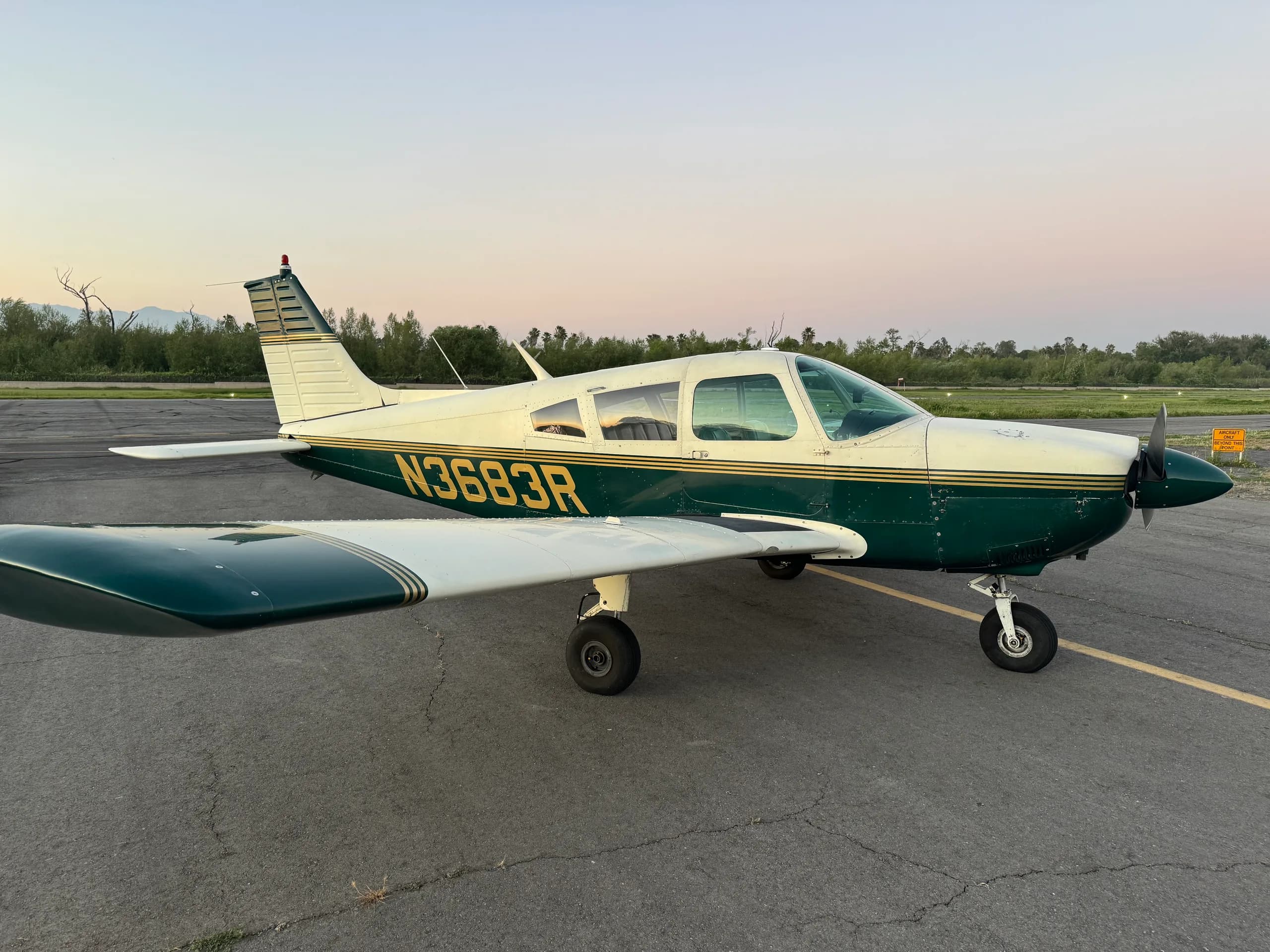 A green and white single-engine propeller aircraft with tail number N3683R is parked on an asphalt runway at sunset.