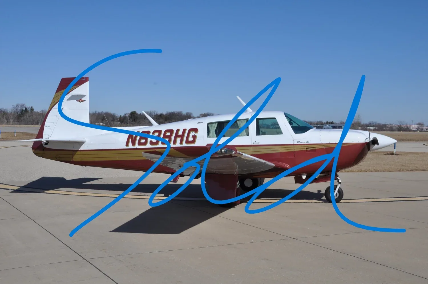 A red and white Mooney 201 aircraft with registration N838HG is parked on an airfield under a clear blue sky, with a large blue 'SOLD' overlay.