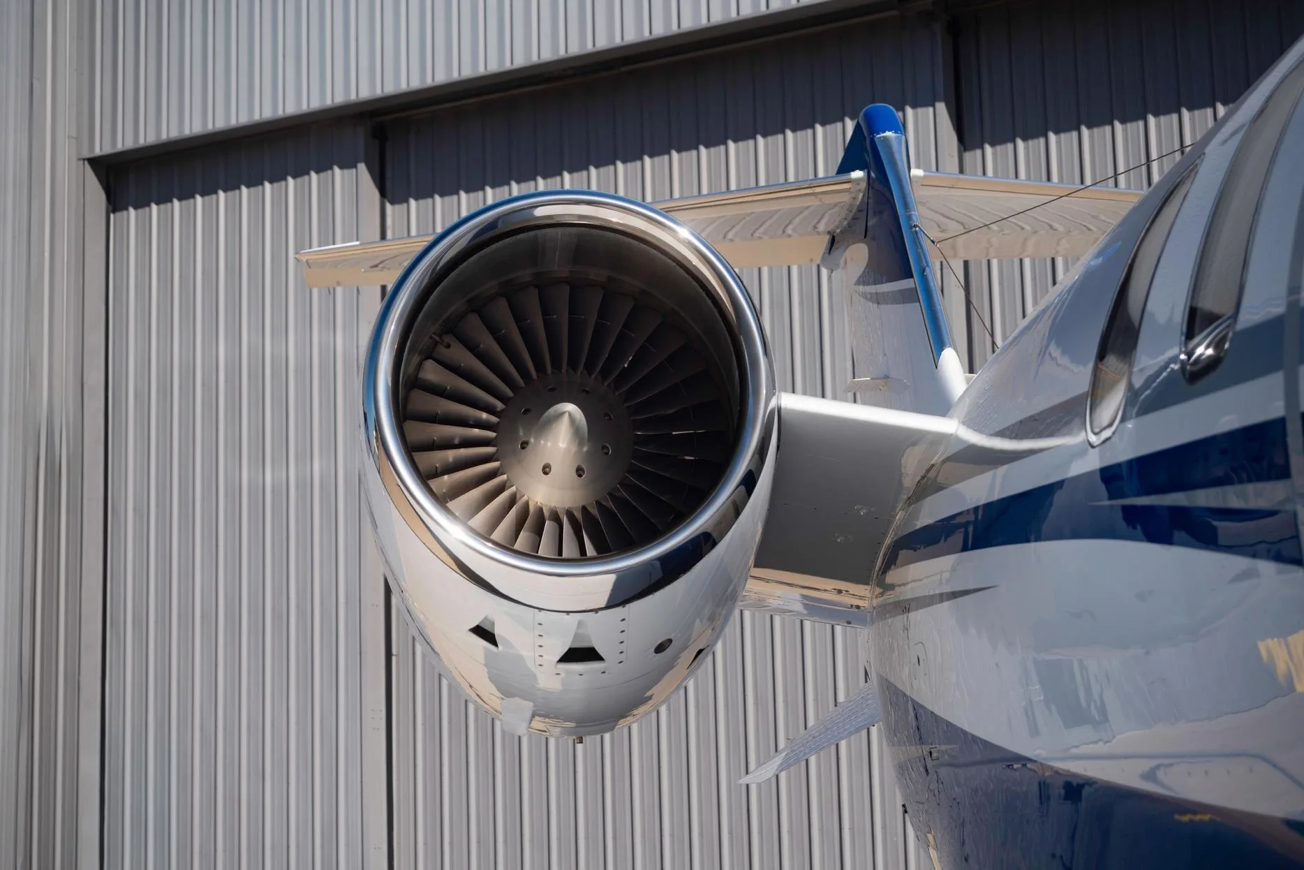 Close-up view of the engine and tail section of a white and blue Learjet 75 business jet against a hangar wall.