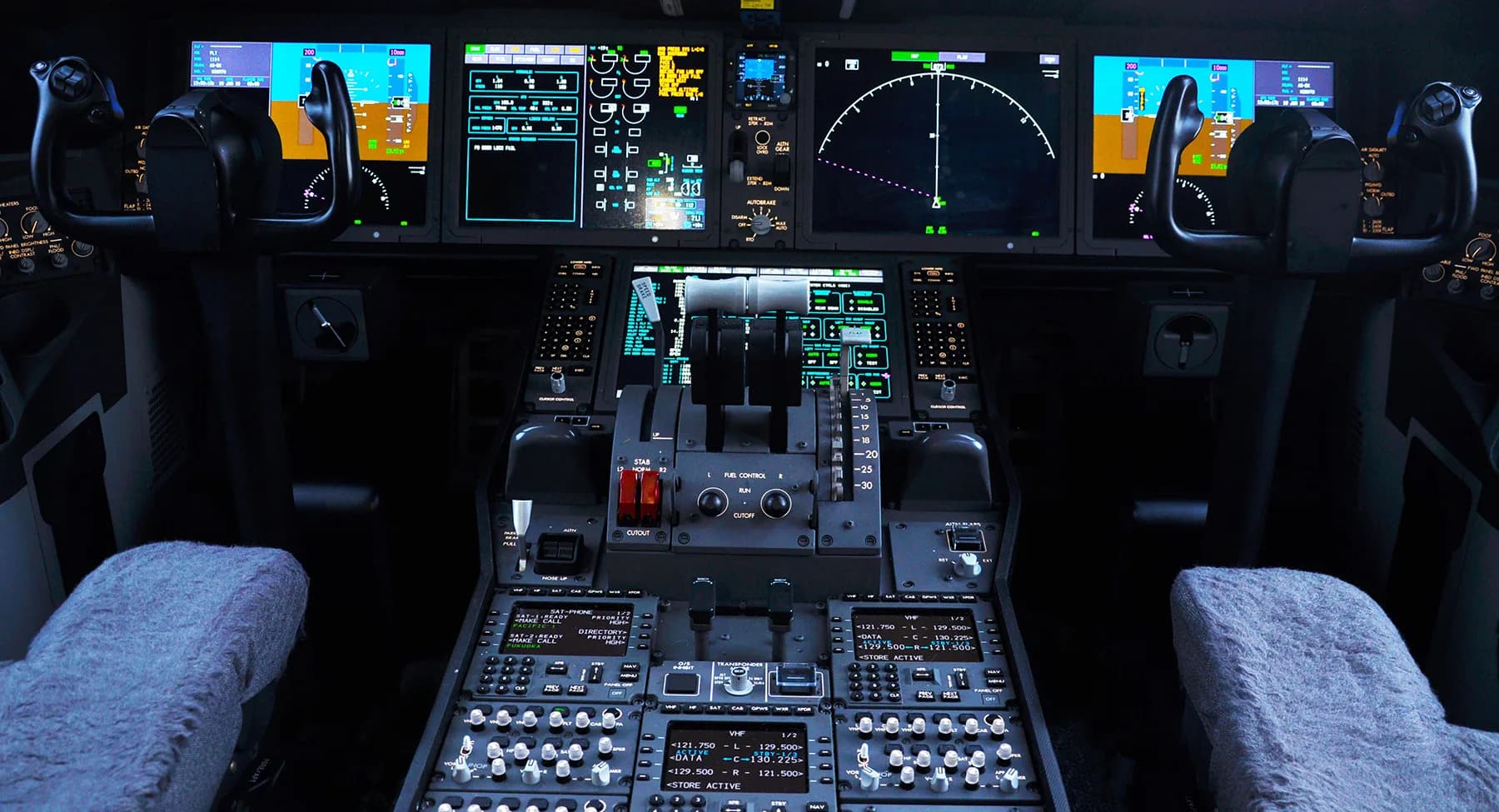 A modern aircraft cockpit with large digital displays, control yokes, and a complex central control panel.