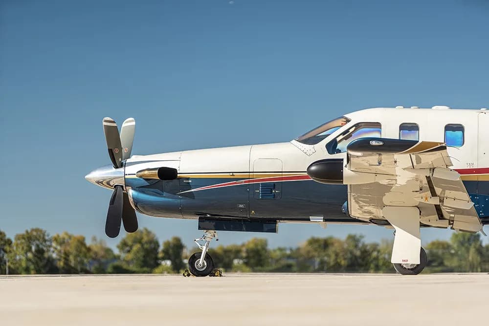 A close-up front-side view of the white, blue, and gold painted turboprop aircraft (N220MA) on an airfield.