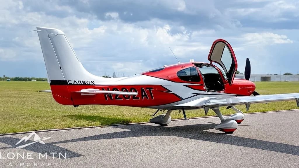 A rear-side view of a red and silver Cirrus SR22T aircraft, registration N282AT, with its doors open, parked on an airfield.
