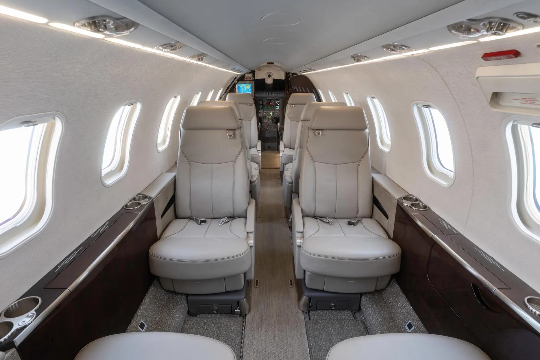 View down the aisle of a private jet cabin showing multiple rows of light gray leather seats.