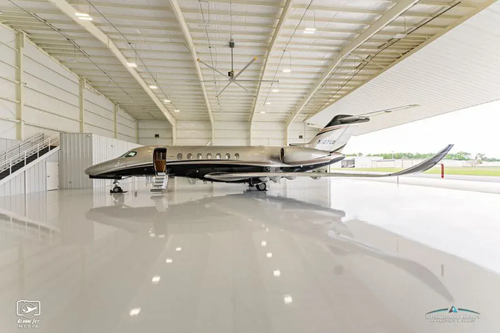 A side view of a grey and black business jet with registration N127CB parked inside a large, brightly lit hangar.