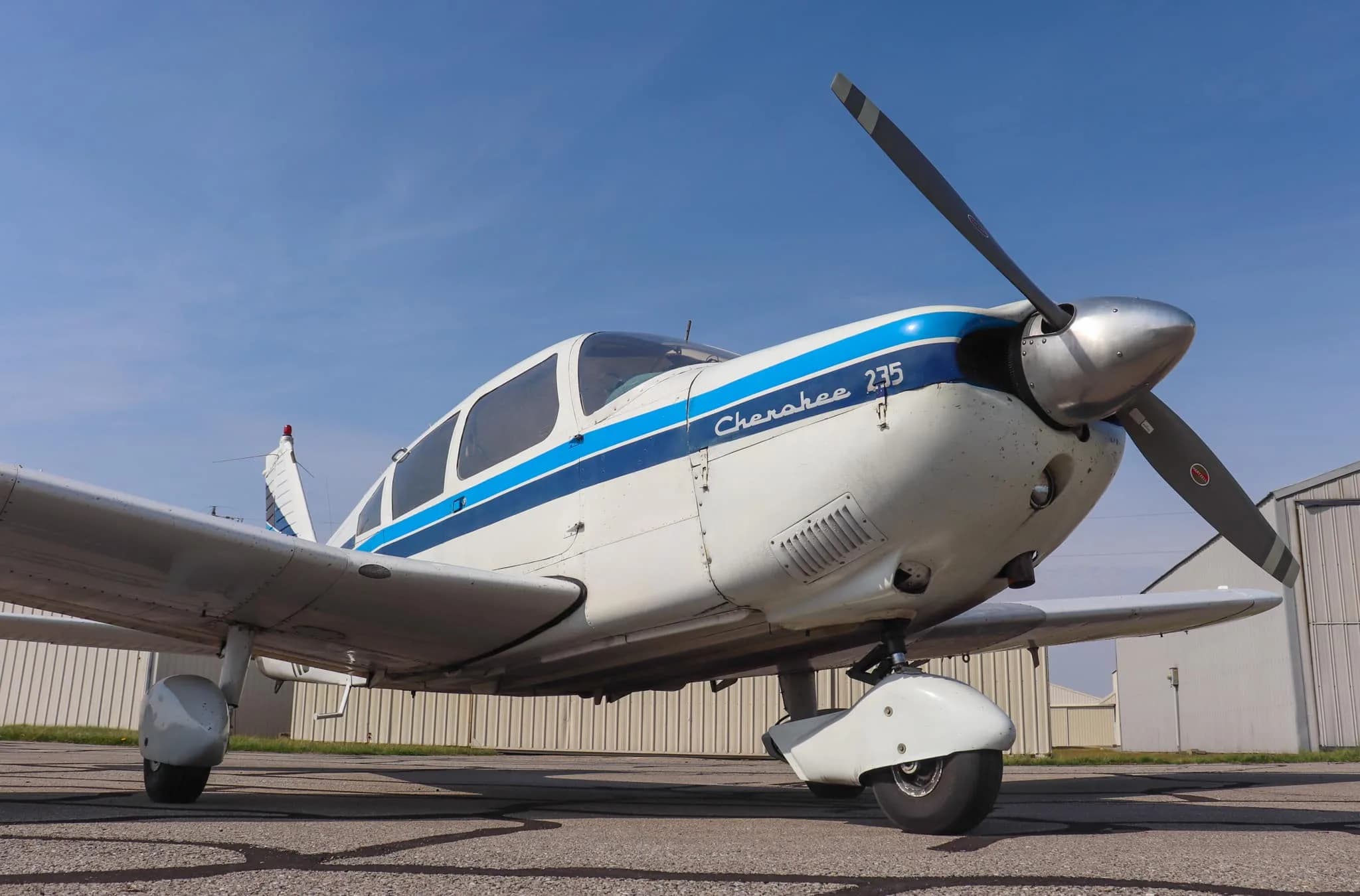A low-angle front view of the white Piper Cherokee 235 aircraft with blue stripes and registration N55032, parked on an asphalt ramp.