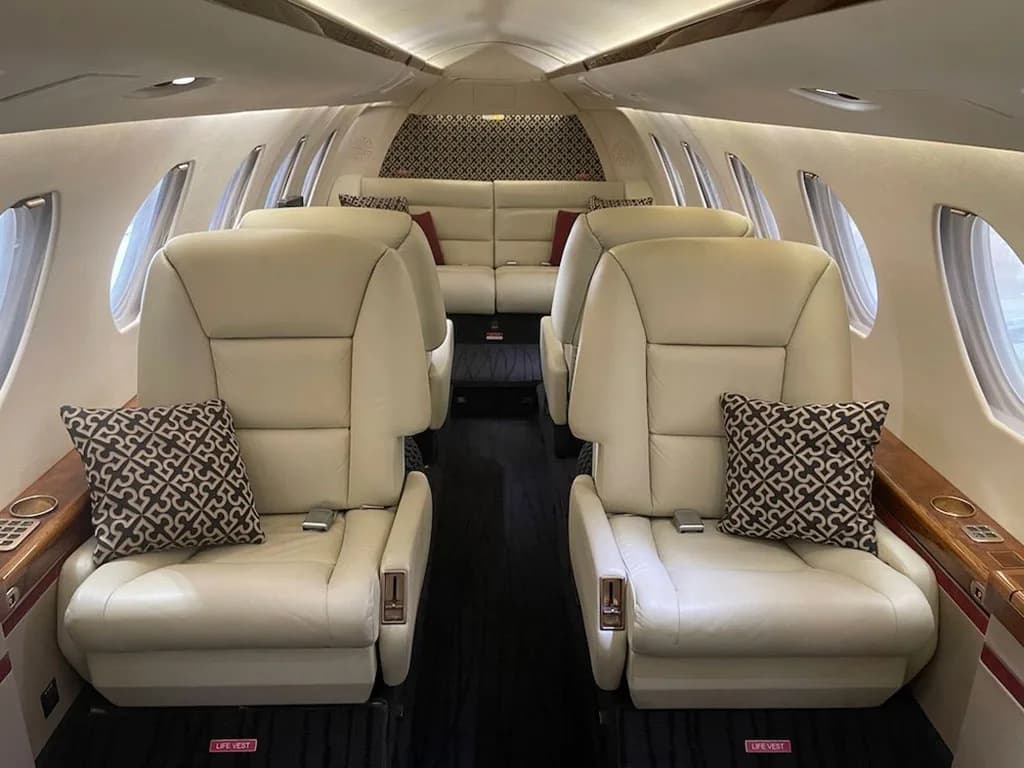 The luxurious interior cabin of a private jet features cream leather seats and patterned pillows.
