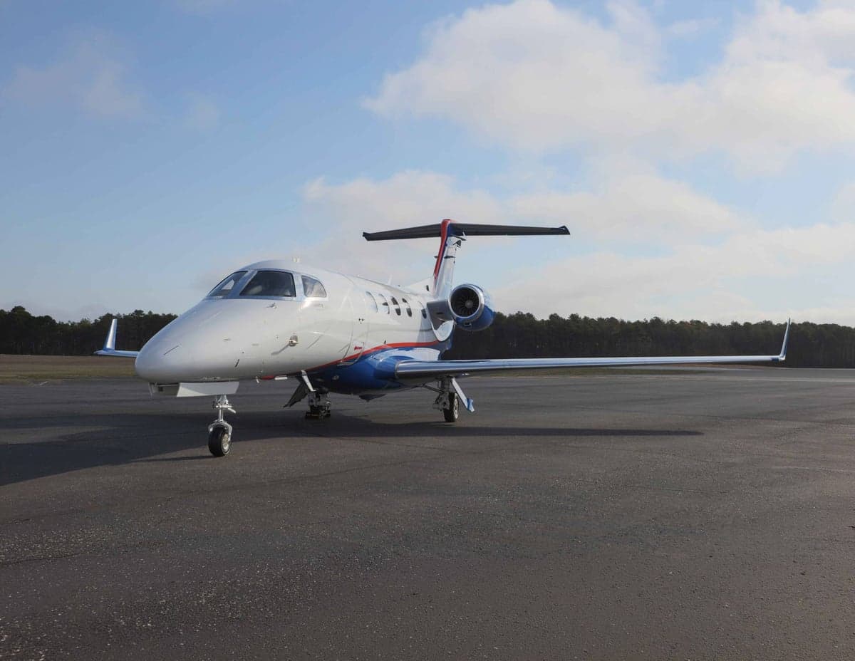 A Phenom 300E aircraft is parked on the tarmac with a blue and white paint scheme.