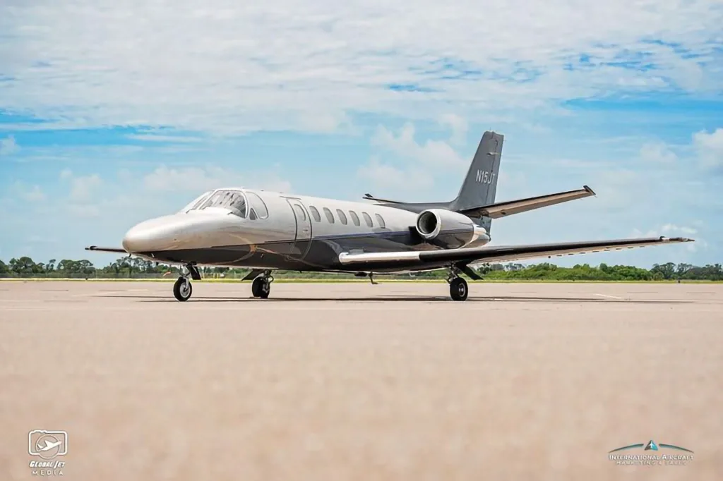 A Cessna Citation X business jet, tail number N15JT, is parked on an airfield under a partly cloudy sky.