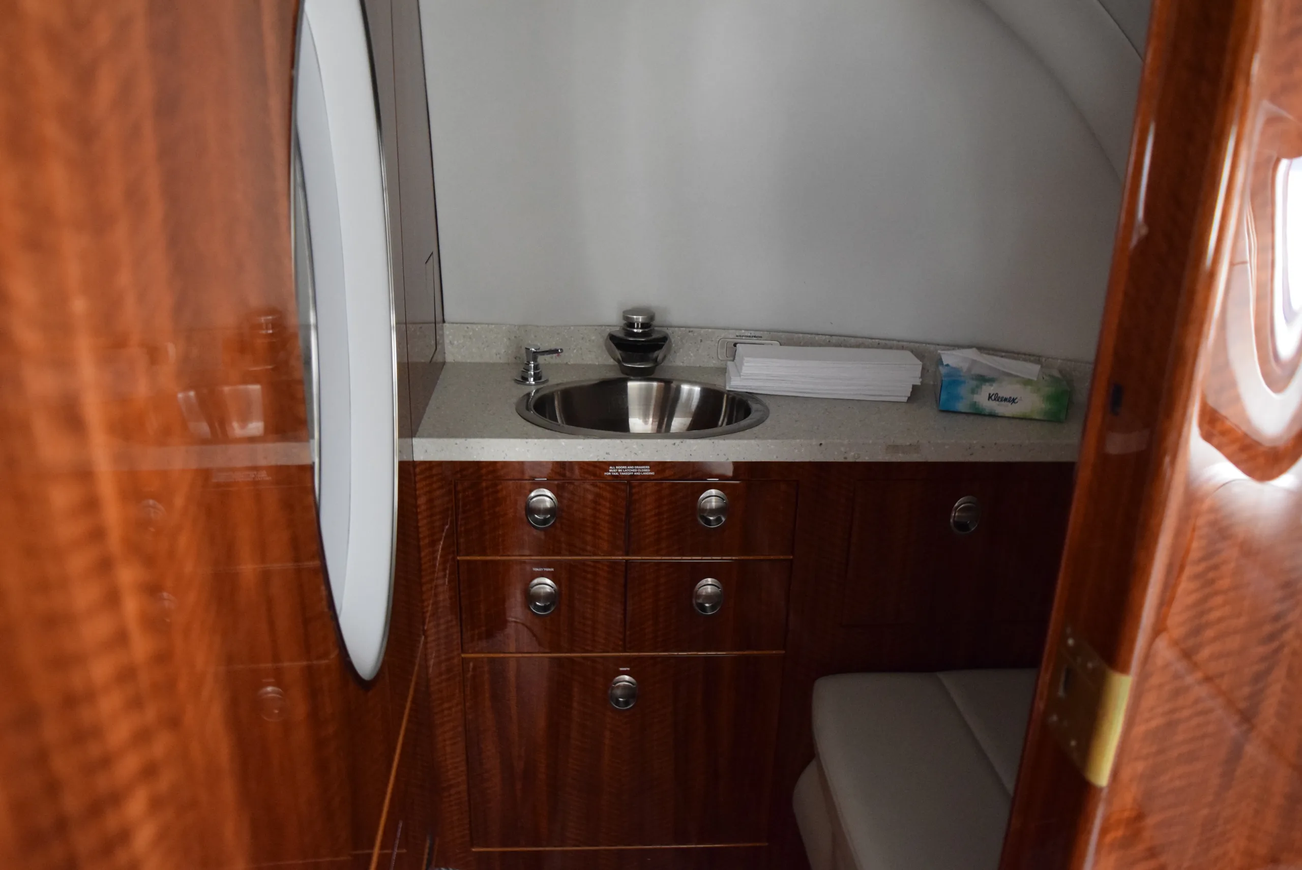 Aircraft lavatory with sink, wood cabinets, and a window.