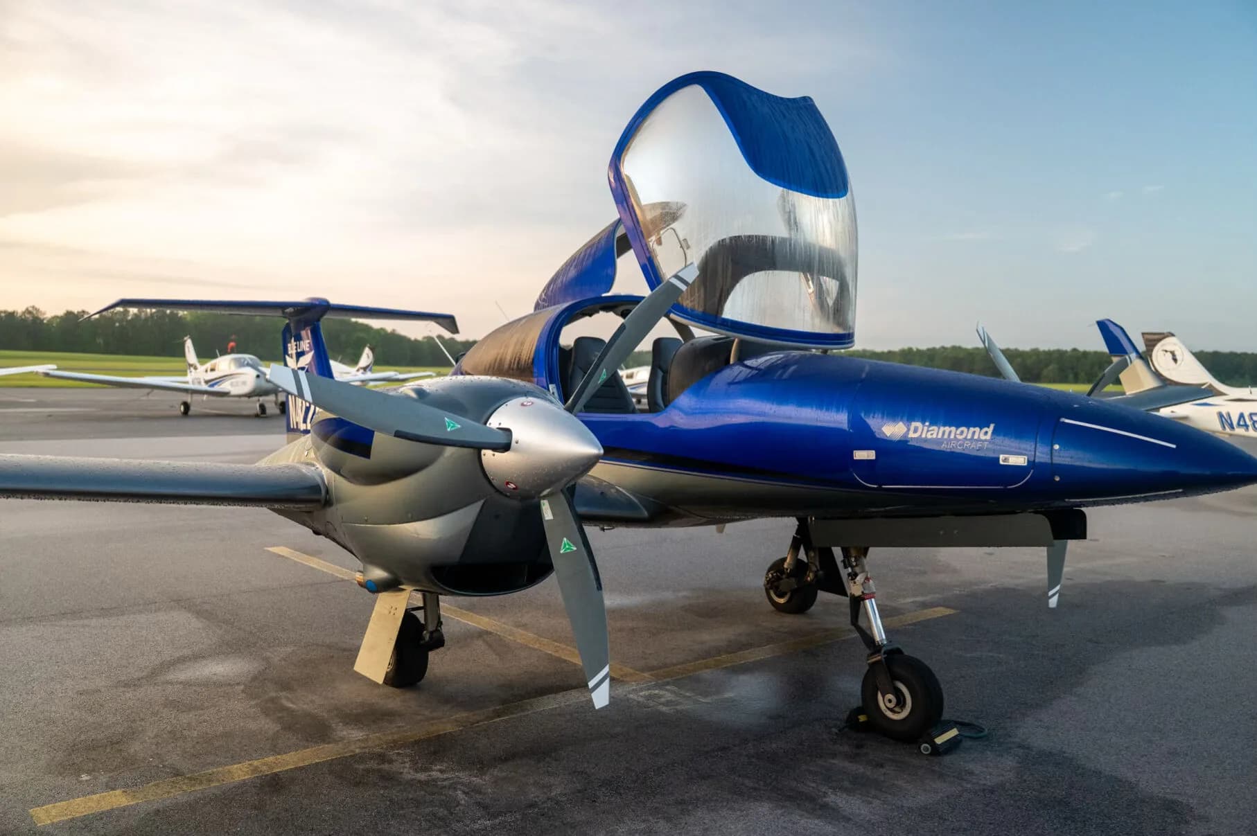Front-side view of the blue and grey Diamond DA42NG aircraft with its canopy open, showing the propeller and engine nacelle.