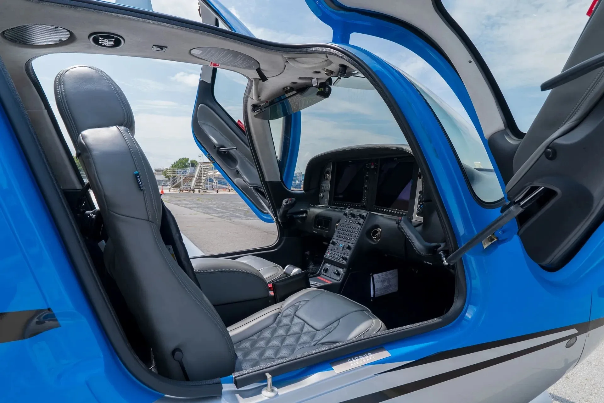 The gray leather interior and cockpit of a Cirrus SR22 aircraft with the doors open.