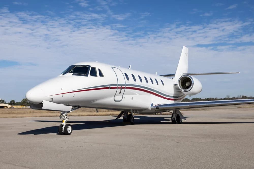 A white business jet with its main cabin door open, parked on an airfield.