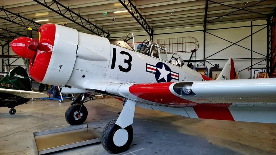 A white and red North American Aviation T-6 Texan aircraft is parked inside a hangar.